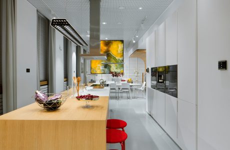 nowoczesne wnętrze Smart od ABB długa biała kuchnia z połączoną wyspa i stołem z dwoma stołkami