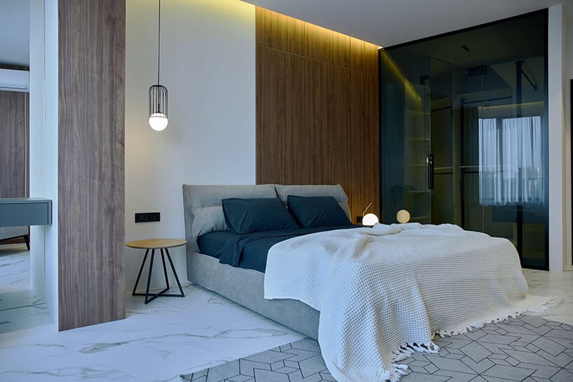 aranżacja sypialni od RB Architects z dużym szarym łóżkiem obok szafy ze szklanymi drzwiami