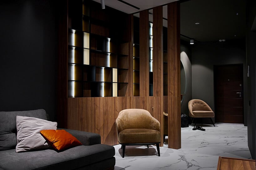 piękny ciemny salon projekty RB Architects z brązową szafką obok szarej sofy jako tło dla niskiego brązowego fotela