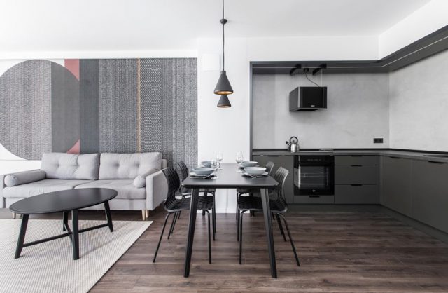 szara kuchnia połączona z salonem z czarnym stołem we wnętrzu apartamentu w gdańskim Dekorian Home projektu Studio Poziom