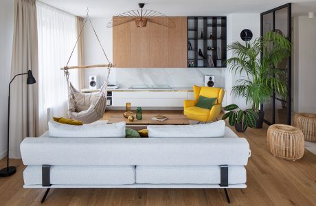 salon w apartamencie z drewnianą podłogą z jasną sofą na tle wiszącego siedziska i żółtego fotelam