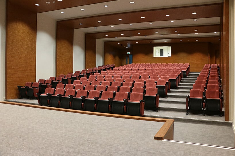 sala wykładowa z czerwonymi fotelami oraz jasno beżową wykładziną