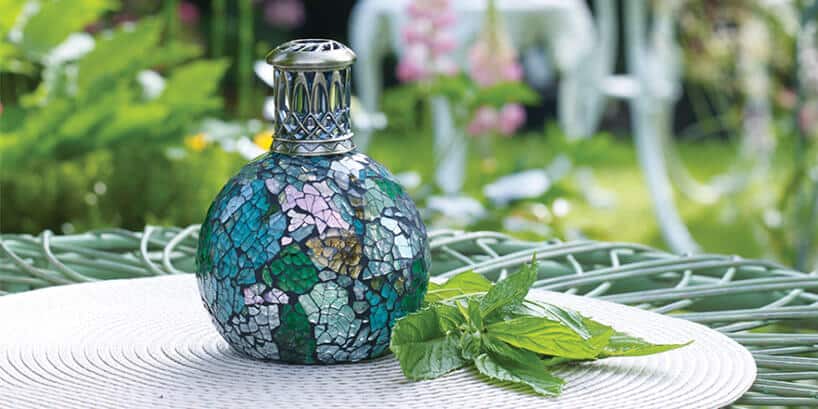 zielono-niebieska lampa zapachowa na stoliku obok kwiatów