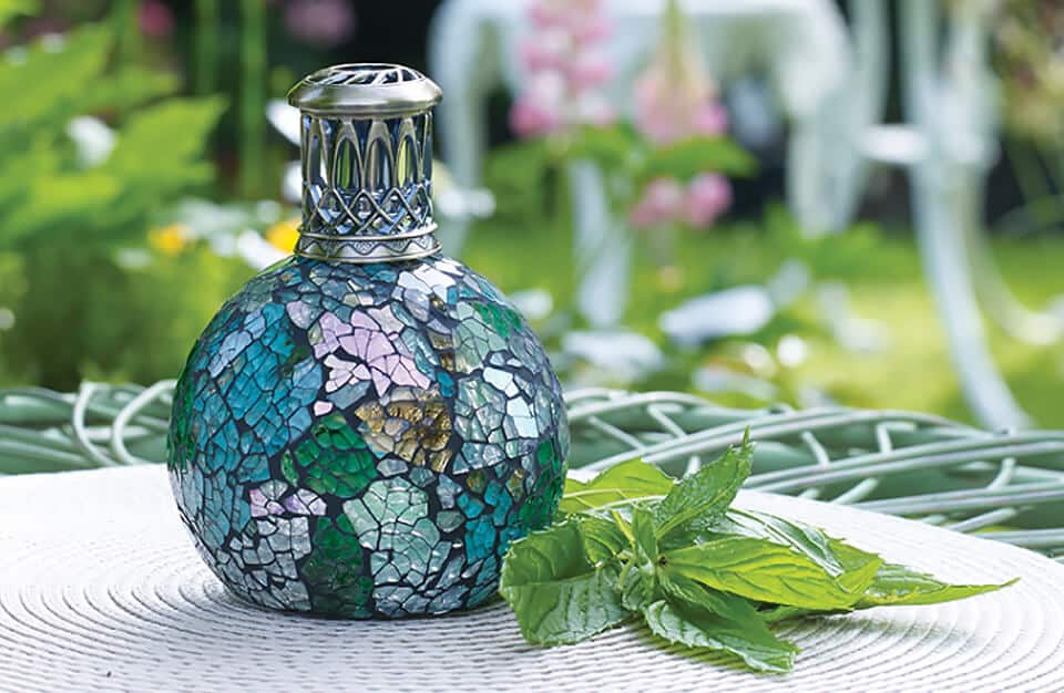 zielono-niebieska lampa zapachowa na stoliku obok kwiatów
