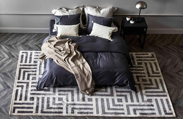 dwuosobowe łóżko na dywanie z motywem labiryntu na ciemnym parkiecie