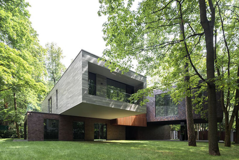 nowoczesny dom w formie prostokątów w kolorach białych i ciemnobrązowych na zielonej działce z drzewami