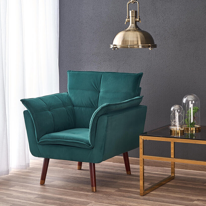 zielony fotel na wysokich drewnianych nogach obok złotego stolika ze szklanym blatem na tle szarej ścianie