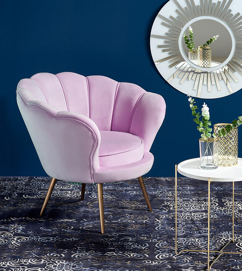 różowy fotel na złotych wysokich nogach na niebieskim dywanie przy białym stoliku pod lustrem z białą ramą