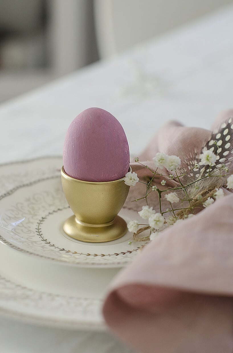 różowe jajko w złotej podstawce na kremowych talerzykach z różową serwetką i dodatkami
