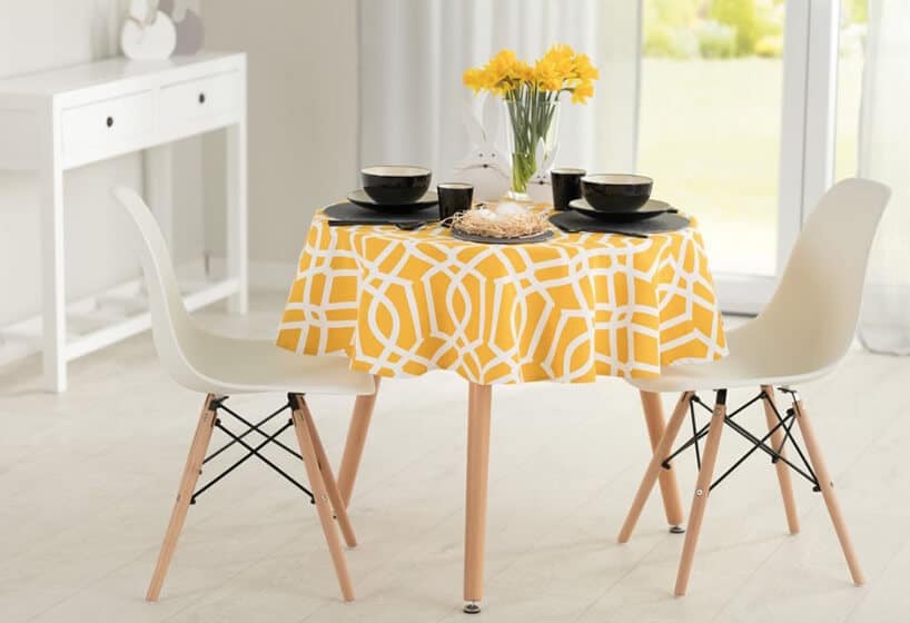 krzesła ze stołem ubranym w kolorowy żółty obrus z zastawą w kolorze czarnym