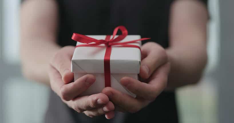 mały prezent zapakowany w biały papier z czerwoną wstążką w rękach kobiety