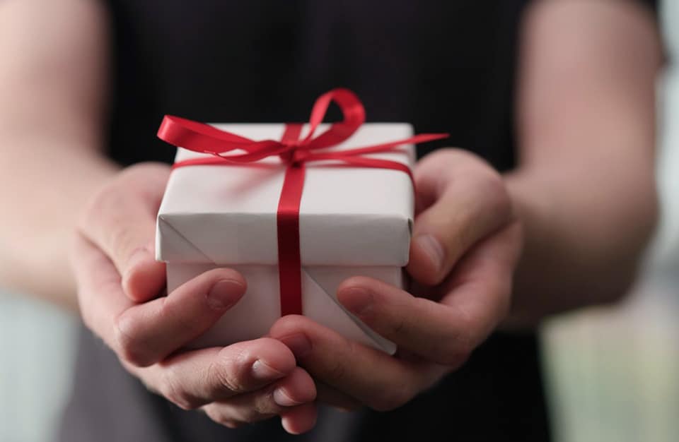 mały prezent zapakowany w biały papier z czerwoną wstążką w rękach kobiety