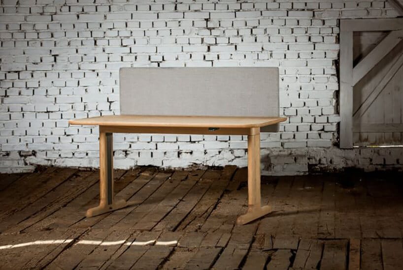 ruchome biurko z jasnym drewnem oraz szarymi pleckami na tle ceglastej ścianie