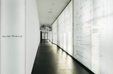 biały korytarz z czarną podłogą ze ścianą wyłożoną powiększonymi zapisami nutowymi Krzysztofa Pendereckiego projektu Nizio Design International