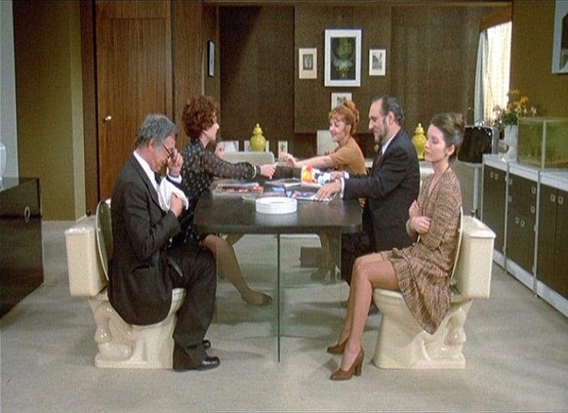 Kadr z filmu „Widmo wolności", ludzie siedzący przy stole na sedesach