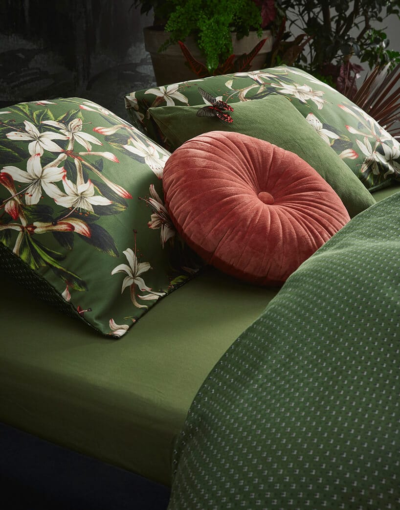 zielone prześcieradło na łóżku z zielonymi poduszkami z kwiatkami oraz jedną ciemno różową okrągłą poduszką
