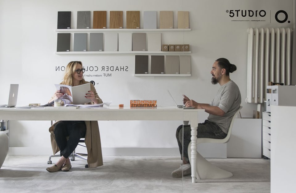 dwie osoby siedzące przy dużym białym biurku w pracowni projektowej