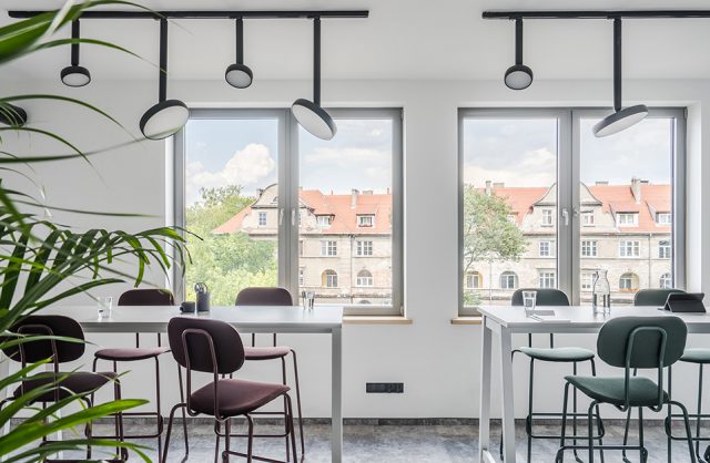nowoczesna przestrzeń biurowa MDD Work Together białe wyższe biurka z krzesłami na tle okien z widokiem na kamienice