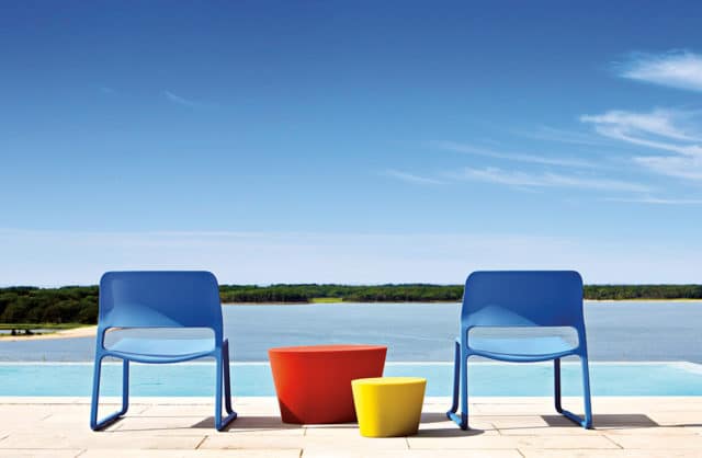 dwa niebieskie krzesła obok dwóch cylindrycznych stolików na tle basenu i lasu w oddali