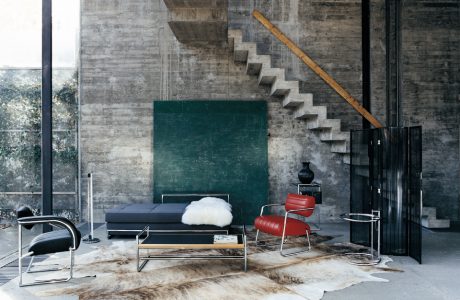 łóżko i dwa fotele z metalowymi szkieletami w wysokim wnętrzu z surowym betonowym klimatem