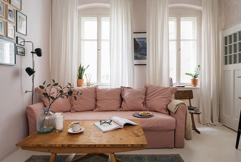 drewniany stolik na tle jasno różowej sofy na tle dwóch wysokich podwójnych okien