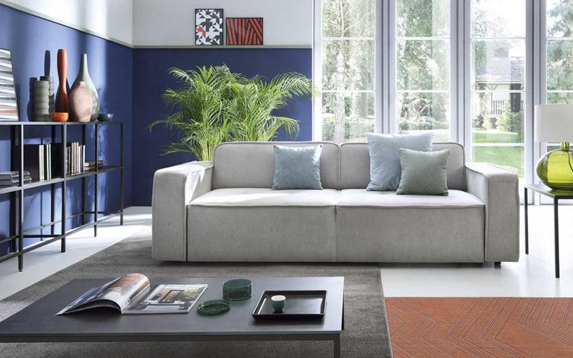 elegancka minimalistyczna jasno szara sofa Modo od Gala Collezione na tle niebieskiej ściany w salonie