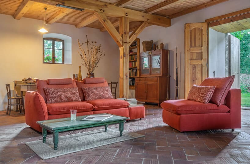 pomarańczowy system modułowy Merida od Gala Collezione obok zielonego niskiego stolika w eleganckim salonie z drewnianm sufitem i drewnianymi słupami