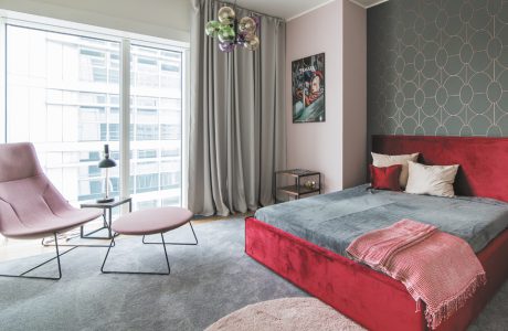 wnętrze apartamentu na Złotej 44 z dużym czerwonym łóżkiem na tle szarej ściany ze złotym wzorem i różowym fotelem