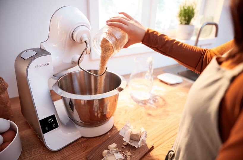nowoczesny planetarny robot kuchenny MUM5 od Bosch na drewnianym blacie kuchennym podczas wsypywania brązowego cukru do miski