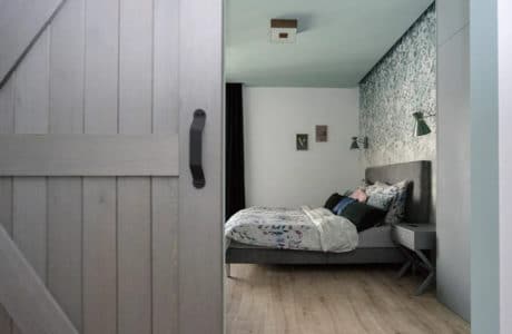 srebrno-szare drzwi przesuwne z desek z czarną klamką i łóżkiem w tle
