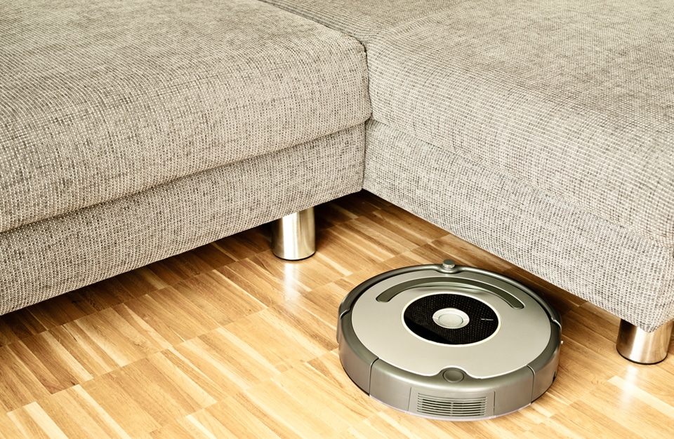 automatyczny okrągły robot sprzątający na drewnianej podłodze przy szarej sofie