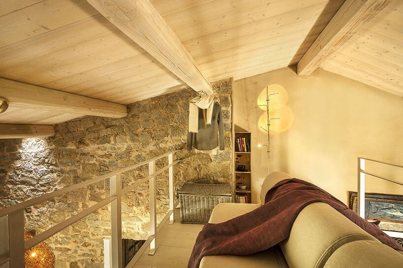 nowoczesne lampa stojąca Wa Wa od Catellani&Smith na antresoli z sofą na tle kamiennej ściany i pod drewnianym odsłoniętym sufitem
