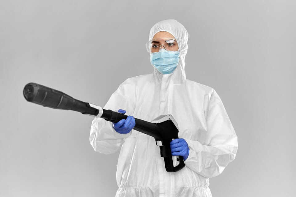 mężczyzna w białym stroju ochronnym i rękawiczkach ochronnych z ozonatorem