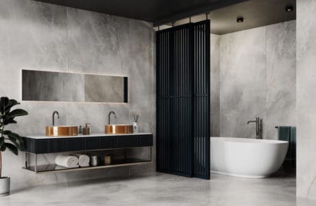 łazienka z metalową ścianką w kolorze czarnym odgradzającą wannę przy betonowych kaflach z białymi wzorami oraz miedzianymi umywalkami