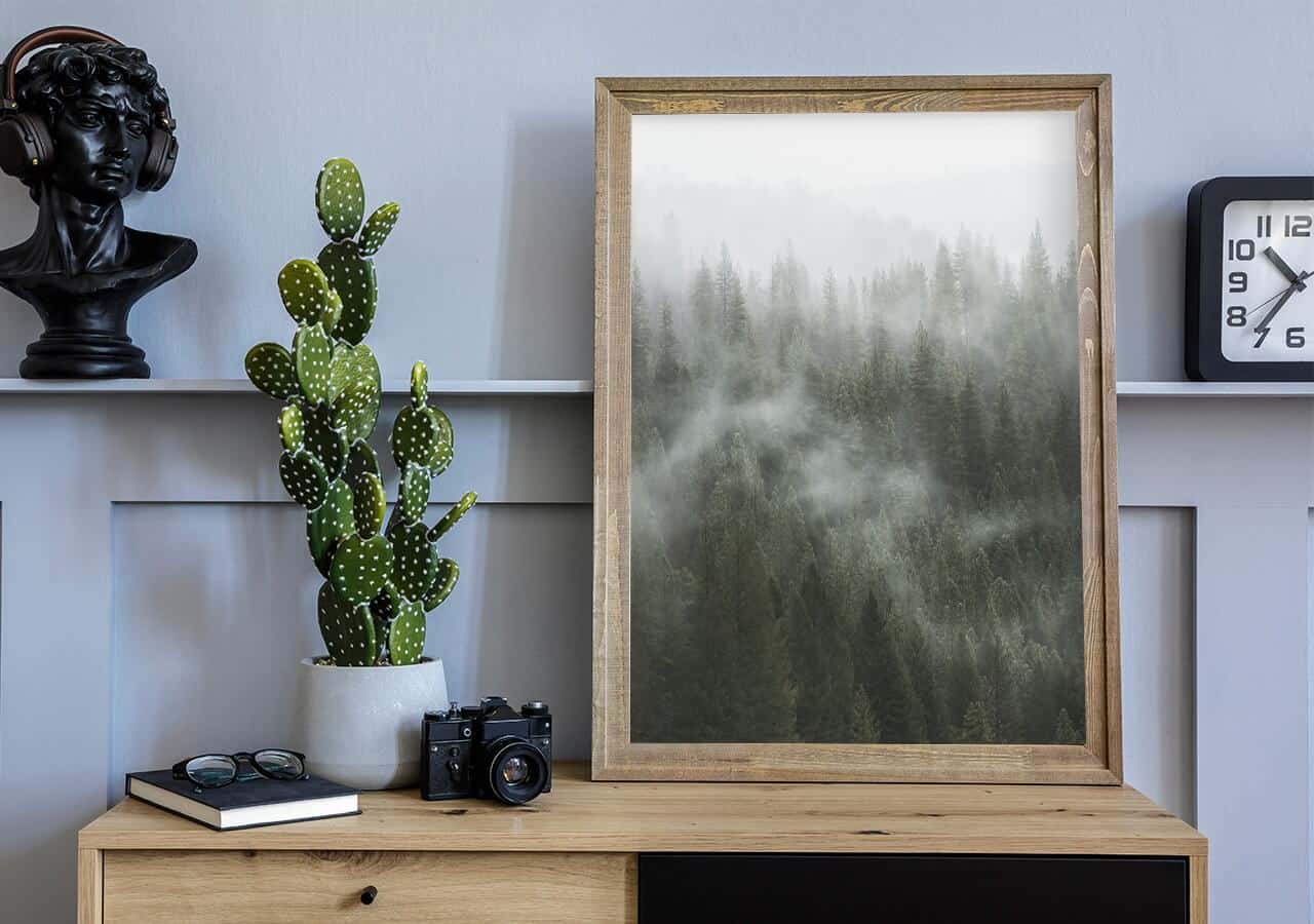 plakat z lasem oparty o biurko , na którym stoi kaktus
