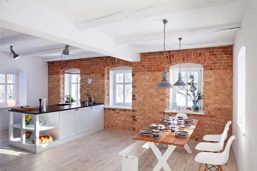 biała kuchnia połączona z salonem o ścianami z odsłoniętej cegły
