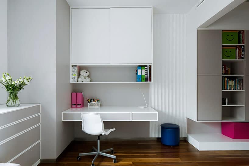 elegancki biały pokój dziecięcy z podwieszanym biurkiem pod białą szafką obok biało szarych szafek i komody