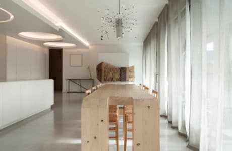 salon z białą aranżacją oraz długimi zasłonami oraz nietypowym wysokim drewnianym stołem