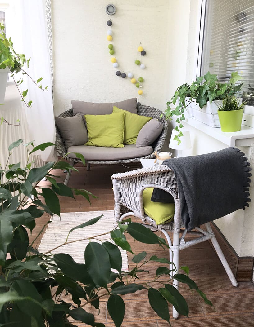 mały balkon w bloku z szerszym fotelem pod ścianą i krzesłem przy drzwiach i dużą liczbą roślin w doniczkach