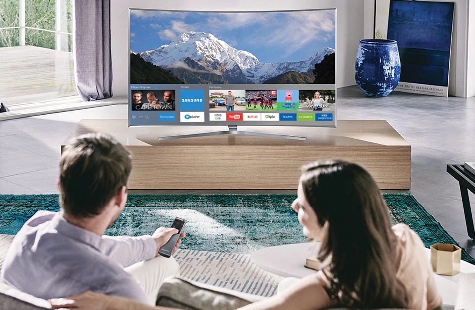 para siedząca na sofie przed dużym telewizorem Samsung z funkcją Smart TV