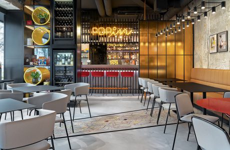 wnętrze restauracji POP in projektu Sikora Wnętrza czarne stoliki z szarymi krzesłami na tle baru z neonem POPin