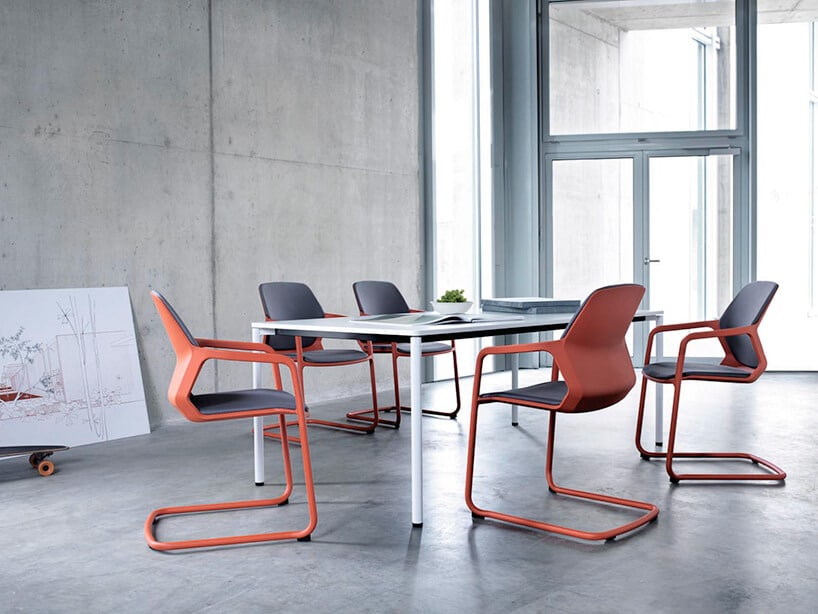pięć nowoczesnych krzeseł Metrik od Wilkhahn czerwony stelaż z szarym siedziskiem i oparciem przy białym stole w szarym betonowym wnętrzu