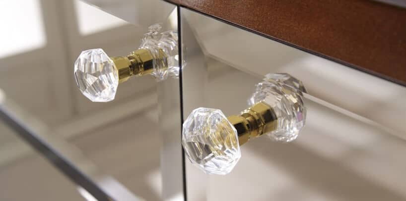 dwa kryształowe uchwyty na złotych mocowaniach na szklanym froncie szafki