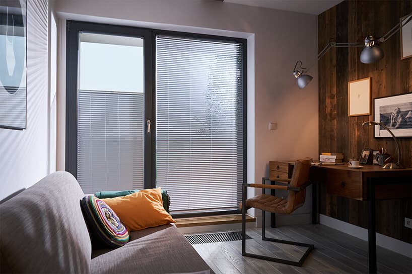 elegancki mały gabinet z drewnianym biurkiem obok dużego okna z szarymi dwukierunkowymi osłonami okiennymi od ANWIS