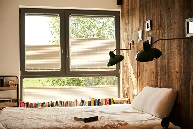 sypialnia ze ściana wyłożoną starym drewnem na tle okna z beżowymi dwukierunkowymi osłonami okiennymi od ANWIS