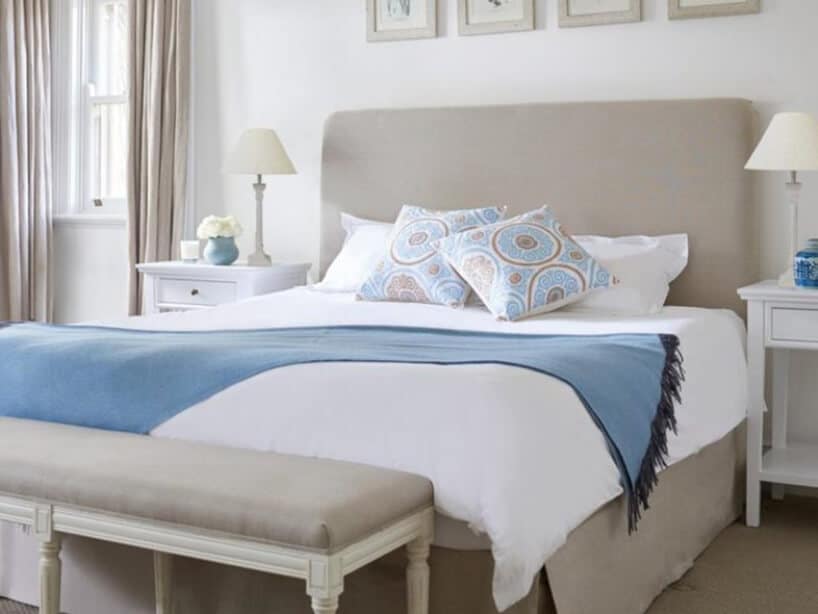 duże lekko szare łóżko z białą pościelą oraz niebieskawą narzutą na nim