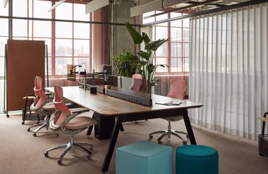 aranżacja biura open space z dużym biurkiem podzielonym n cztery stanowiska z czterem różowymi ergonomicznymi krzesłami