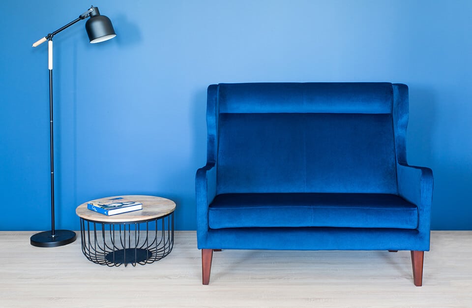 niebieski fotel obok stolika z prętów i drewnianego blatu na tle niebieskiej ściany
