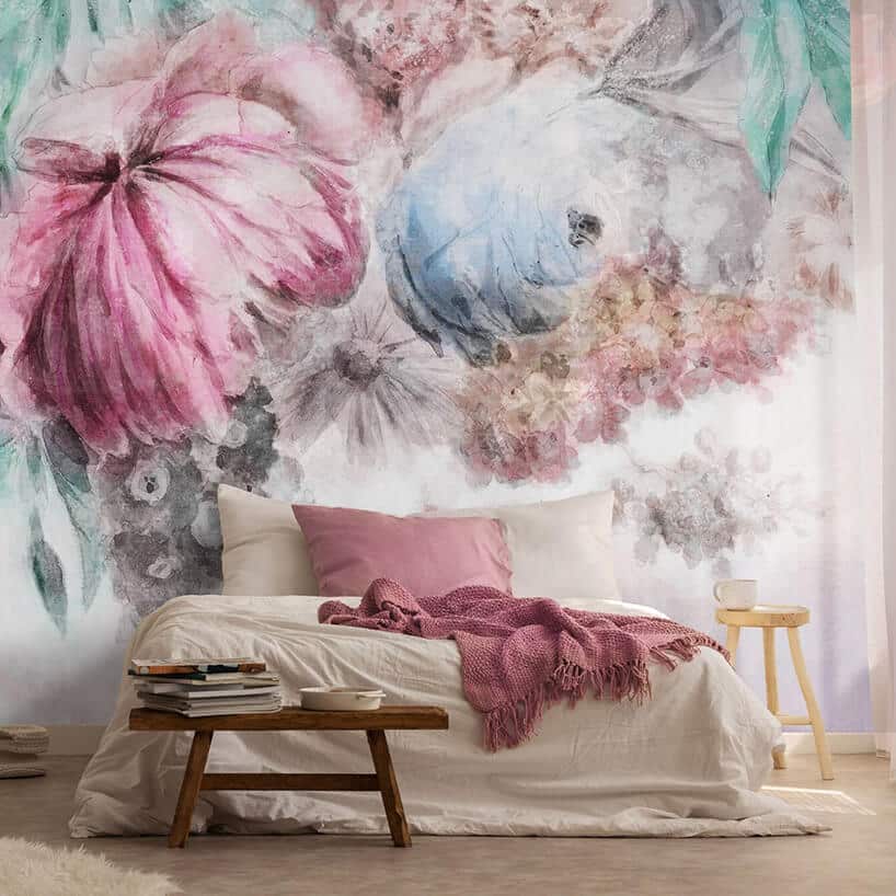 duże łóżko z beżową pościelą i różową narzutą na tle tapety z kwiatowym pastelowym motywem