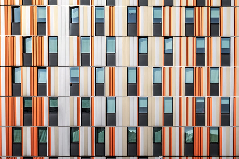 zdjęcie eelewacji nowoczesnego budynku z czarnymi oknami i pomarańczowo biało beżową elewacją